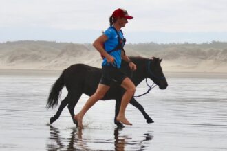A woman running along a beach with a mini horse.