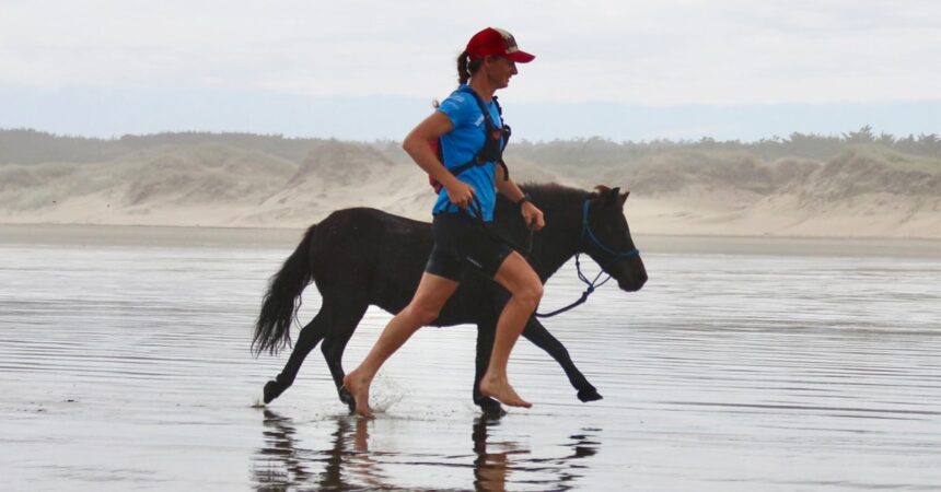 A woman running along a beach with a mini horse.