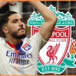Rayan Cherki poses with his arms in the air in front of Liverpool club crest.