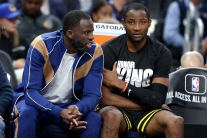 Draymond Green #23 (left) speaks to Jonathan Kuminga #00 of the Golden State Warriors on the bench during a game against the New Orleans Pelicans.